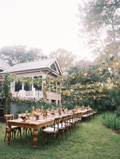 an outdoor dining table set up in front of a house with flowers and greenery