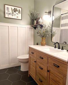 a white toilet sitting next to a sink in a bathroom under a large mirror and wooden cabinets