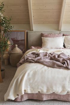 a bed with white and pink linens in a bedroom next to a potted plant