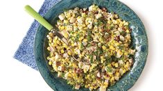 a blue bowl filled with corn and meat on top of a table next to a green spoon