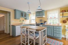 a kitchen with blue cabinets and yellow walls, wooden flooring and two pendant lights over the island