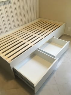 a white bed with drawers underneath it on the floor in front of a striped wall