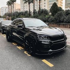 two black cars are parked on the side of the road in front of palm trees