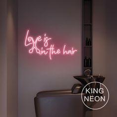 a neon sign that says love is in the hair on a wall above a chair