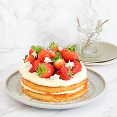 a cake with strawberries and whipped cream on top sits on a plate next to a glass of water