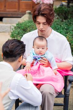 a man sitting in a chair holding a baby while another person holds the baby up to her chest