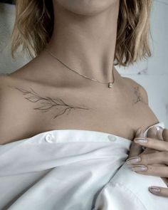 a woman wearing a white dress with a feather tattoo on her chest