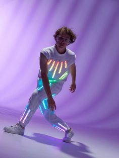 a man in white shirt and light up leggings posing for the camera with purple background