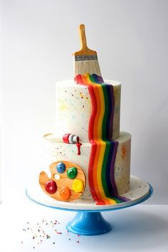 a multi - tiered cake decorated with paintbrush and rainbows