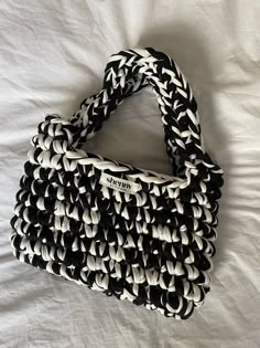 a black and white handbag laying on top of a bed with the handles down