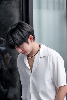 a young man with black hair wearing a white shirt looking down at his cell phone