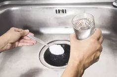 two hands holding a spoon over a metal sink with water and ice cubes in it