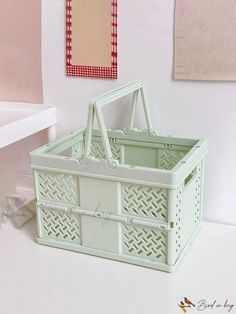 a white plastic basket sitting on top of a table next to a wall with pictures above it