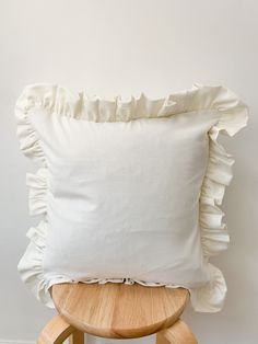 a white pillow with ruffled edges on a wooden stool next to a white wall