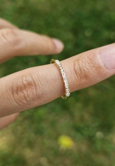 a woman's hand with a diamond ring on top of her finger and grass in the background