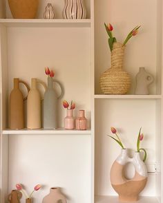 some vases and flowers are on shelves in a room with white walls or shelving