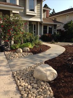 a house that has some rocks on the ground in front of it and bushes near by