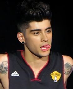 a young man with tattoos on his arm and chest wearing a black jersey, looking at the camera