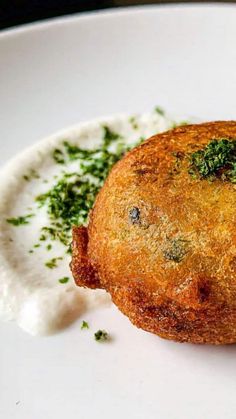 a piece of food on a white plate with sauce and parsley sprinkled around it