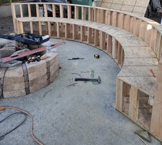 a curved wooden bench sitting on top of a cement floor next to a pile of tools