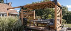 a patio with a table and chairs under a wooden pergoline structure on the side of a house