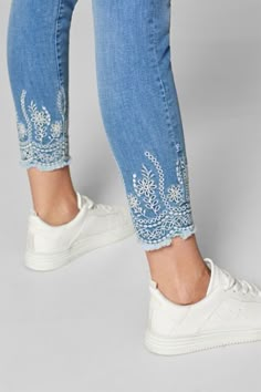 a woman's legs in jeans and white sneakers with embroidered details on them, both from the waist down