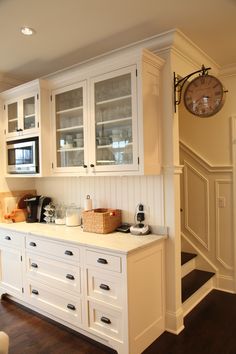 a kitchen with white cupboards and drawers next to a clock mounted on the wall