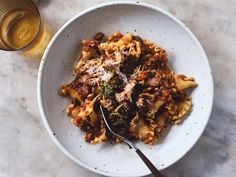 a white bowl filled with pasta and broccoli next to a glass of beer