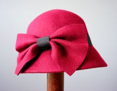 "DESCRIPTION * vintage hat from 1990s * Bucket style: round high crown with sloping downturned stiff brim * made with wool felt fabric * in deep red with a tint of purple * hatband is wrapped with a black grosgrain ribbon and embellished with a red bow * the bow can be worn to the side or to the back * tag reads \"One Size Body 100% Wool, Ribbon 100% Polyester\" CONDITION * Hat is in good clean condition with one spot of the insect bite mark, shown in the last photo. SIZE Hat circumference 22.5\ Vintage Cloche Hat For Winter, Vintage Cloche Hat With Short Brim For Parties, Vintage Winter Fedora For Party, Red Vintage Mini Hats With Curved Brim, Vintage Short Brim Party Hats, Vintage Winter Party Fedora, Retro Pink Wide Brim Hat, Retro Red Party Hat, Red Retro Party Hat