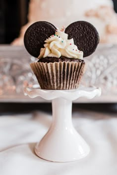 a cupcake with an oreo on top is sitting on a cake stand in front of a wedding cake