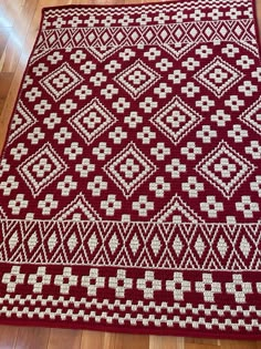 a red and white knitted area rug on the floor with wood floors in the background