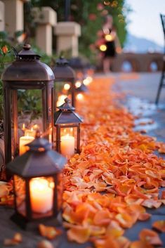 several lanterns are lined up on the ground with leaves all around them and lit by candles