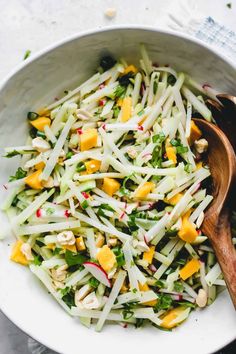 a salad in a white bowl with wooden spoons next to it on a table