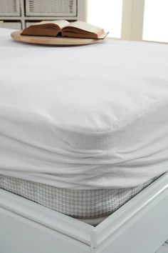 an open book sitting on top of a bed with white sheets and drawers in the background