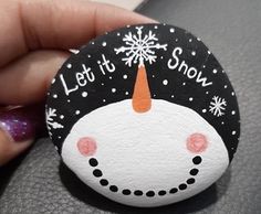 a hand holding a rock with a snowman on it and let it snow written on it