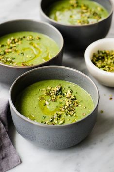 three bowls filled with green soup and garnished with nuts, on a marble surface