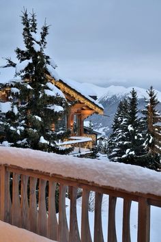 a wooden bench sitting in front of a snow covered mountain side house with lights on