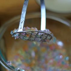 a glass bowl filled with colorful beads and a pair of tongs sticking out of it