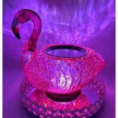 a pink glass candle holder with a flamingo on it's side and purple lights behind it