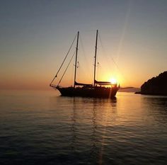 a sailboat in the water at sunset with its sails down and sun shining behind it