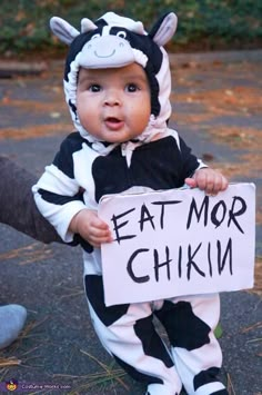 a baby dressed in a cow costume holding a sign that says eat mor chikin