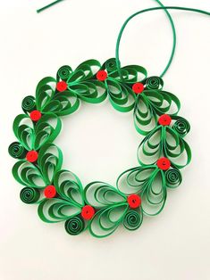 an origami christmas wreath made with green paper and red buttons on a white background