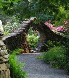 a stone bridge in the middle of a garden filled with flowers and greenery on both sides