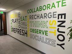 an office hallway decorated with green and black lettering on the wall, along with a plant