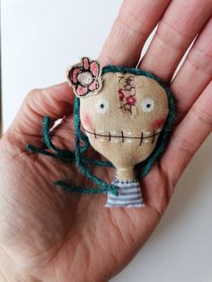 a hand holding a small doll in it's left hand with a flower on its head