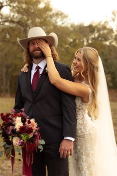 a bride and groom pose for a wedding photo in front of the camera, wearing cowboy hats