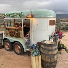 an old fashioned food truck is parked on the side of a dirt road with wine barrels