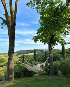 a woman laying in a hammock between two trees on a sunny day,