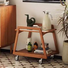 a small wooden shelf with various items on it next to a potted plant and a painting