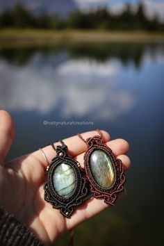 a person is holding some kind of earring in their hand by the water's edge